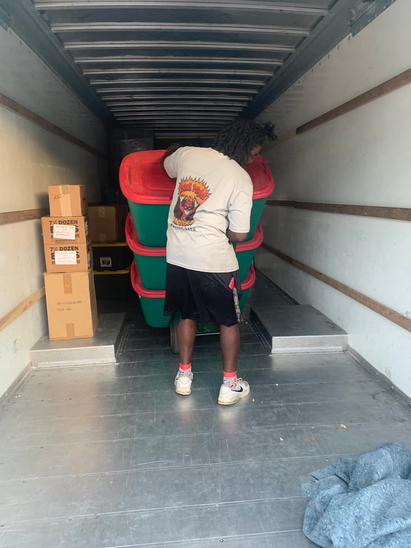 A DynaMight Movers crew member loading stacked storage totes into a moving truck.