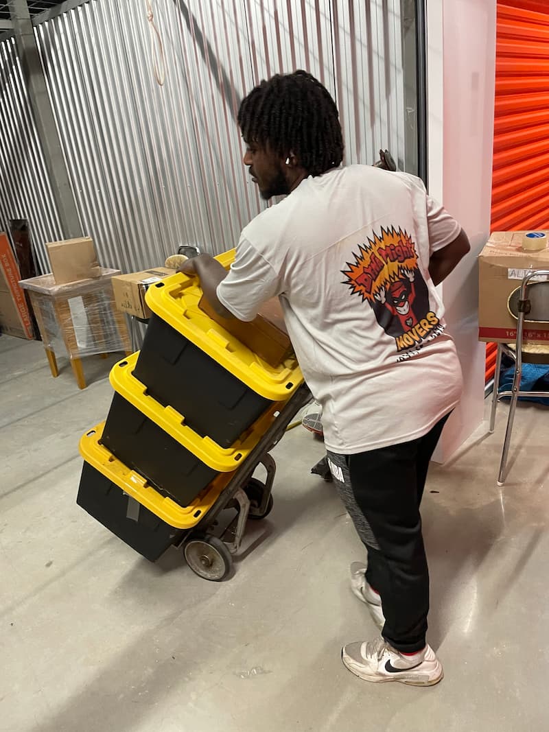 A DynaMight Movers crew member loading stacked storage totes onto a dolly for a long-distance move.